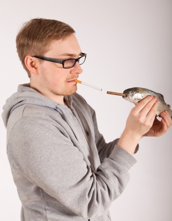 Young man holds a small fish, both are smoking