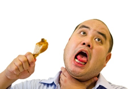 Man appearing to choke on a chicken drumstick he is holding